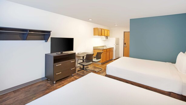 Une chambre d’hôtel comprenant un lit, un bureau avec une chaise, une télévision, une kitchenette et une armoire.