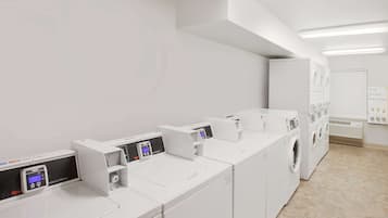 Une buanderie équipée de plusieurs machines à laver et de plusieurs séchoirs, d’une machine à laver industrielle et d’un climatiseur fixé au mur.