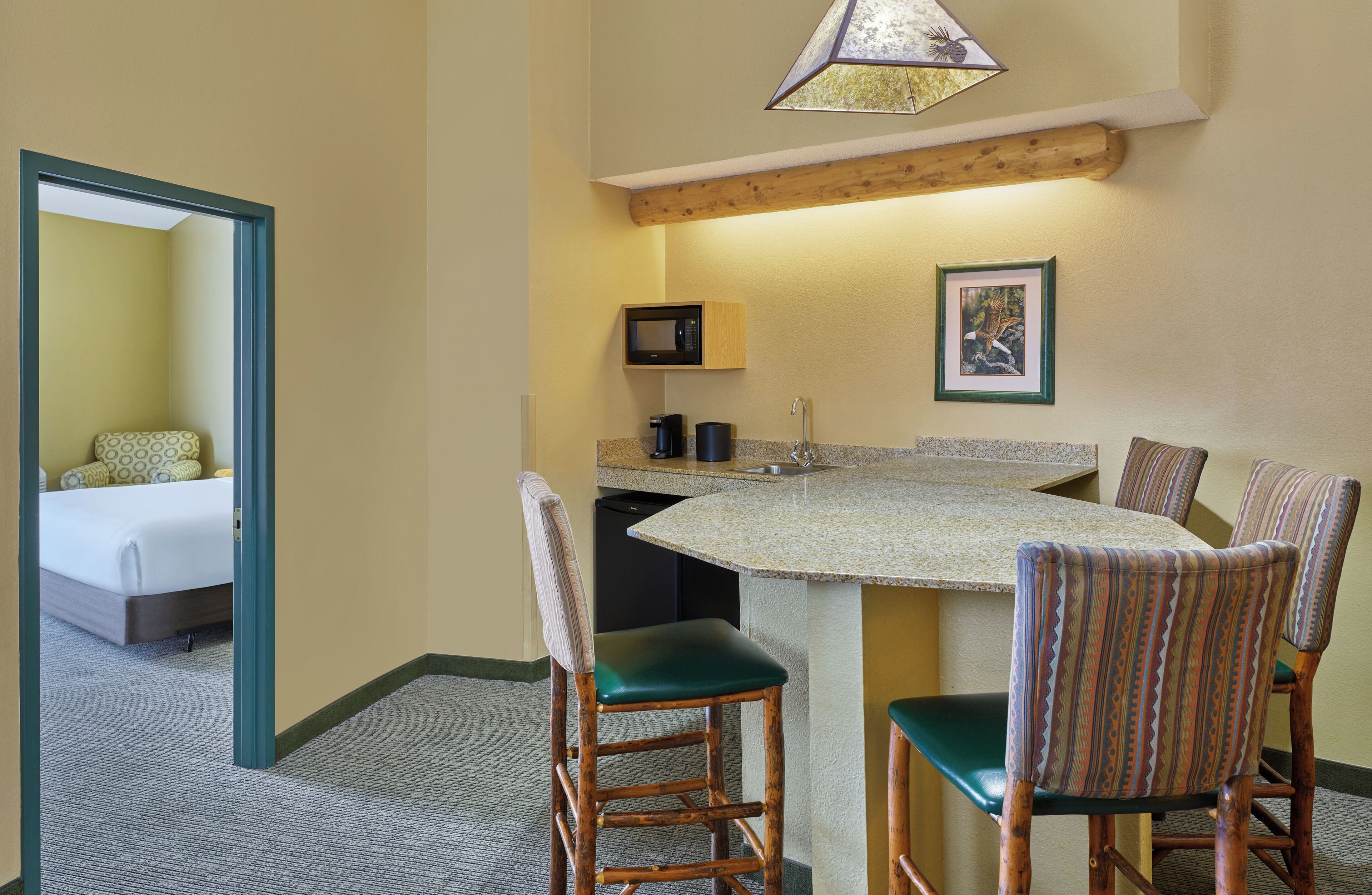 A compact hotel room with a bed, a kitchenette, a dining area with chairs, and a small bathroom.