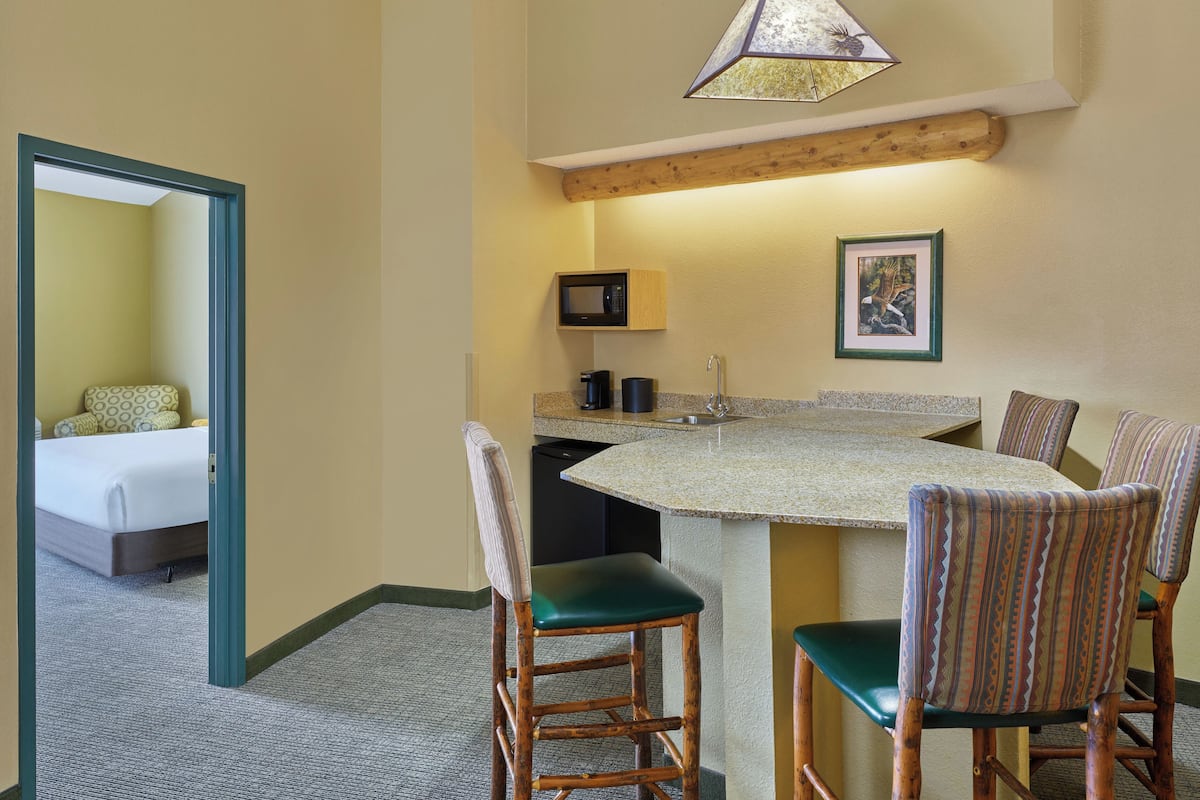 A compact hotel room with a bed, a kitchenette, a dining area with chairs, and a small bathroom.
