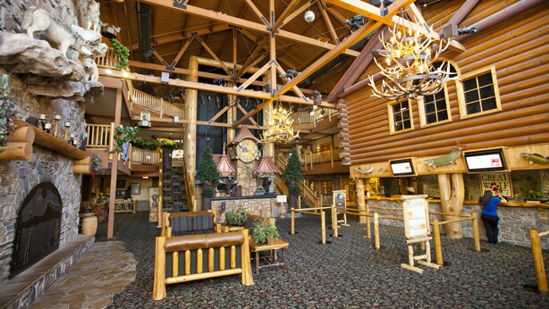 A log cabin interior with a stone fireplace, wooden benches, a chandelier, and a sign reading "Great Wolf."