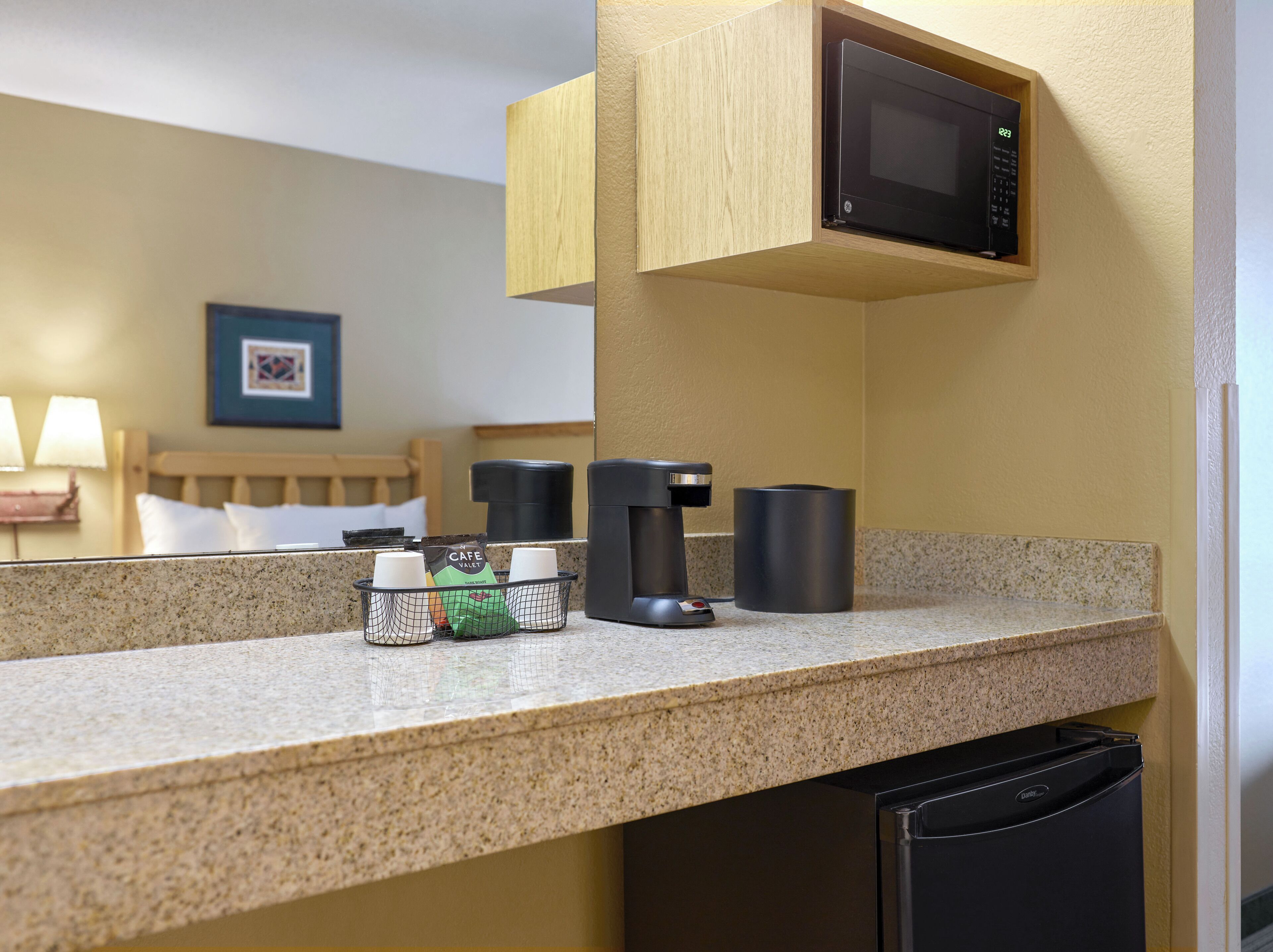 Uma cozinha compacta em hotel, com micro-ondas, máquina de café e dispensador de café.