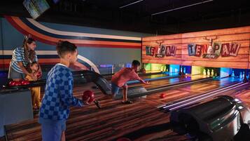 A bowling alley with multiple lanes, a wooden bowling alley sign, and a colorful wall with a wave design.