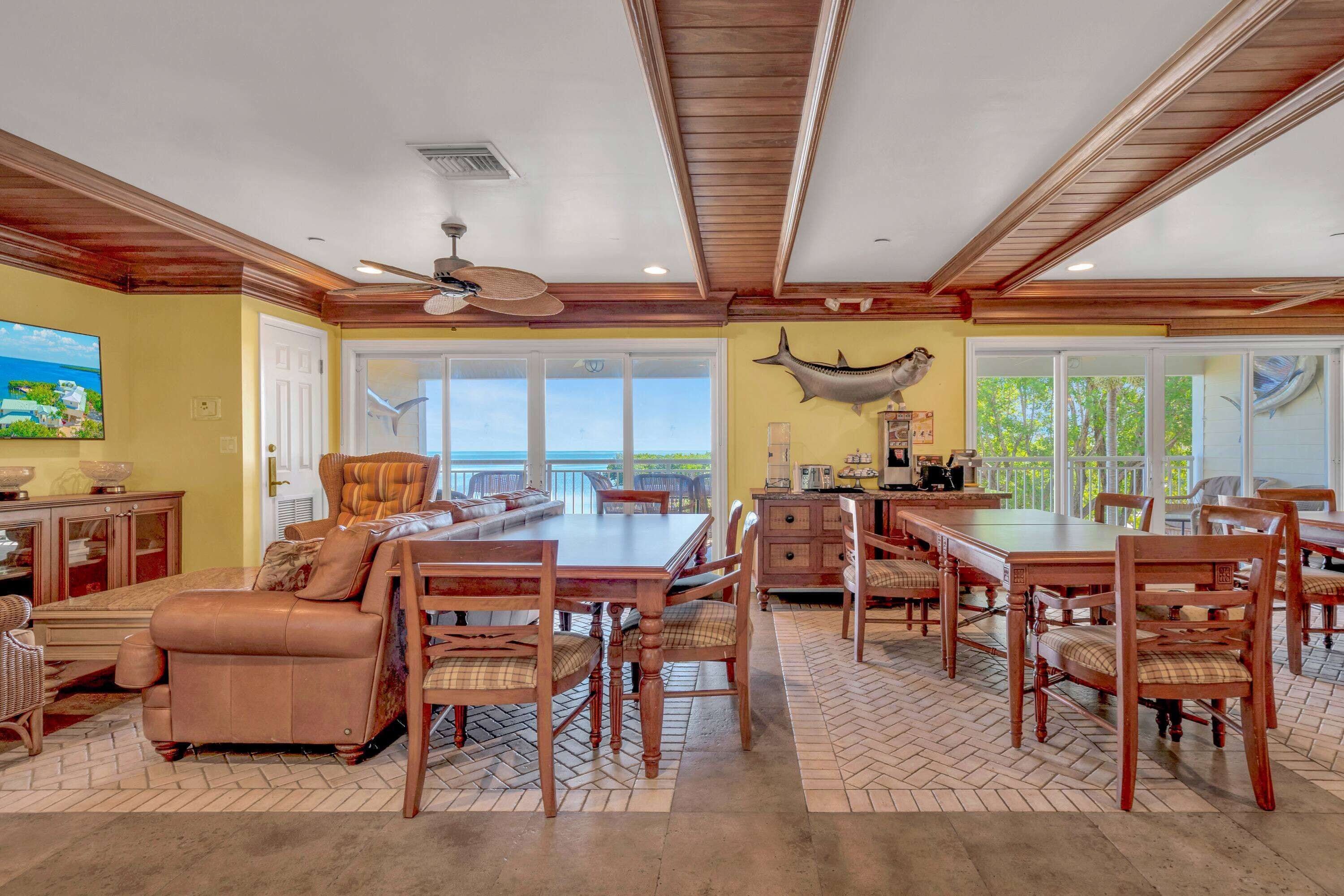A spacious dining area with a large wooden table and chairs, a ceiling fan, and a view of the outdoors.