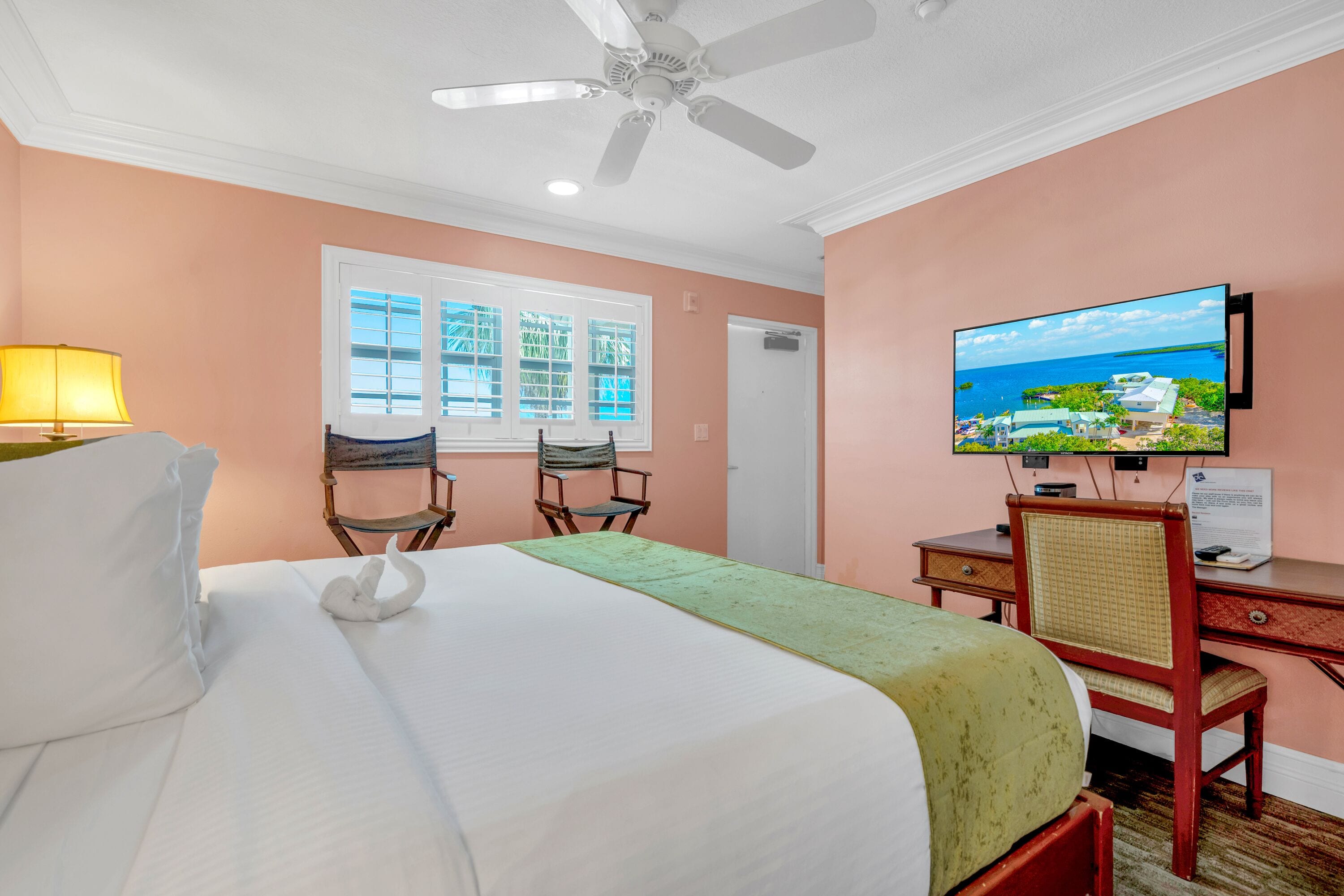 A hotel room with a bed, a desk with a television, a chair, and a window with blinds.