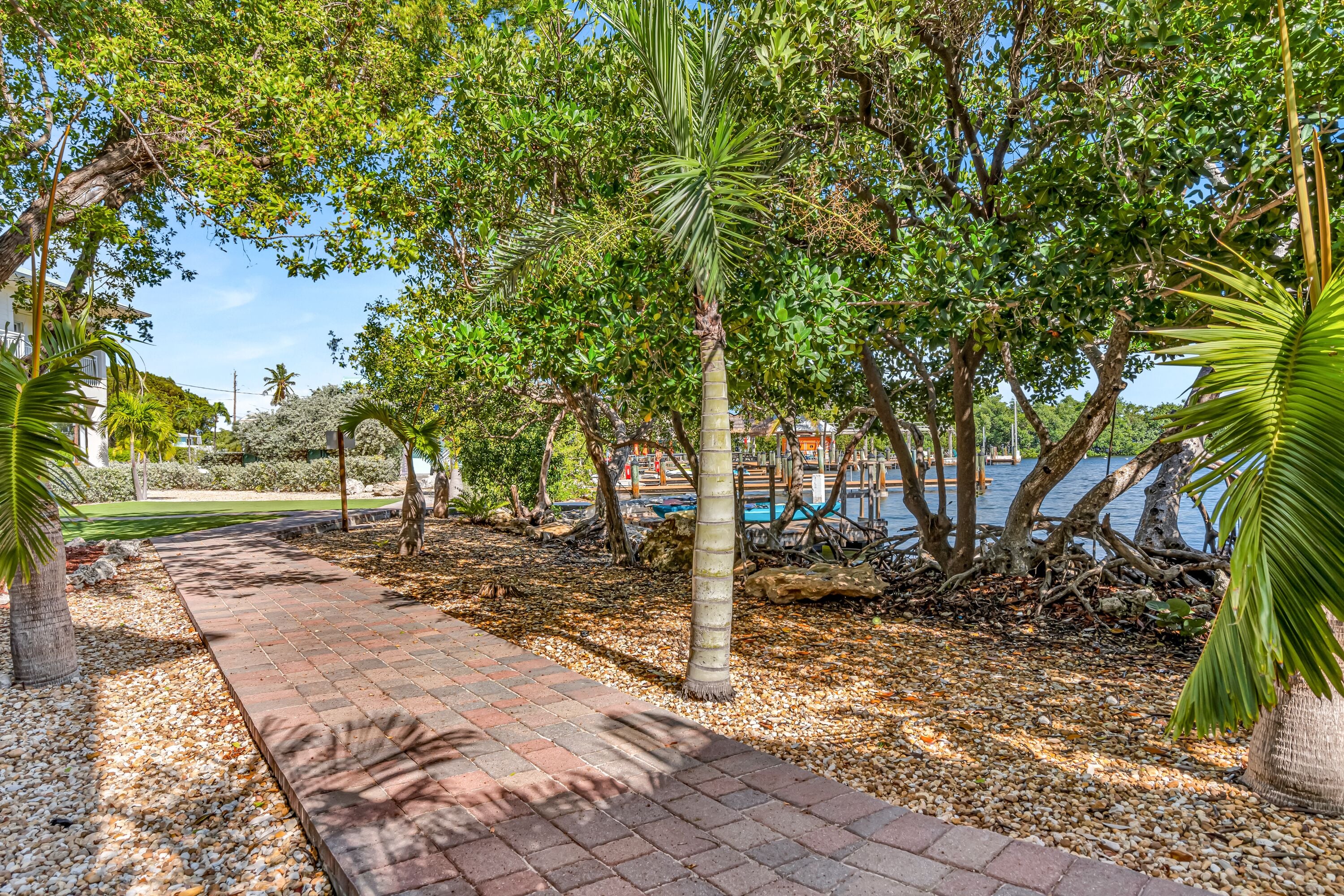 A paved pathway lined with trees and pebbles, leading to a body of water.