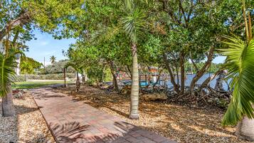 A paved pathway lined with trees and pebbles, leading to a body of water.