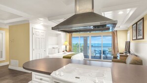 A modern kitchen with a built-in stove, a large island, and a view to a balcony with outdoor seating. - Dove Creek Resort & Marina, Trademark Collection by Wyndham (Key Largo)