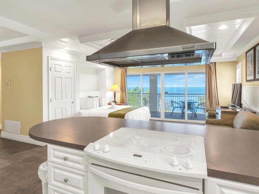 A modern kitchen with a built-in stove, a large island, and a view to a balcony with outdoor seating.