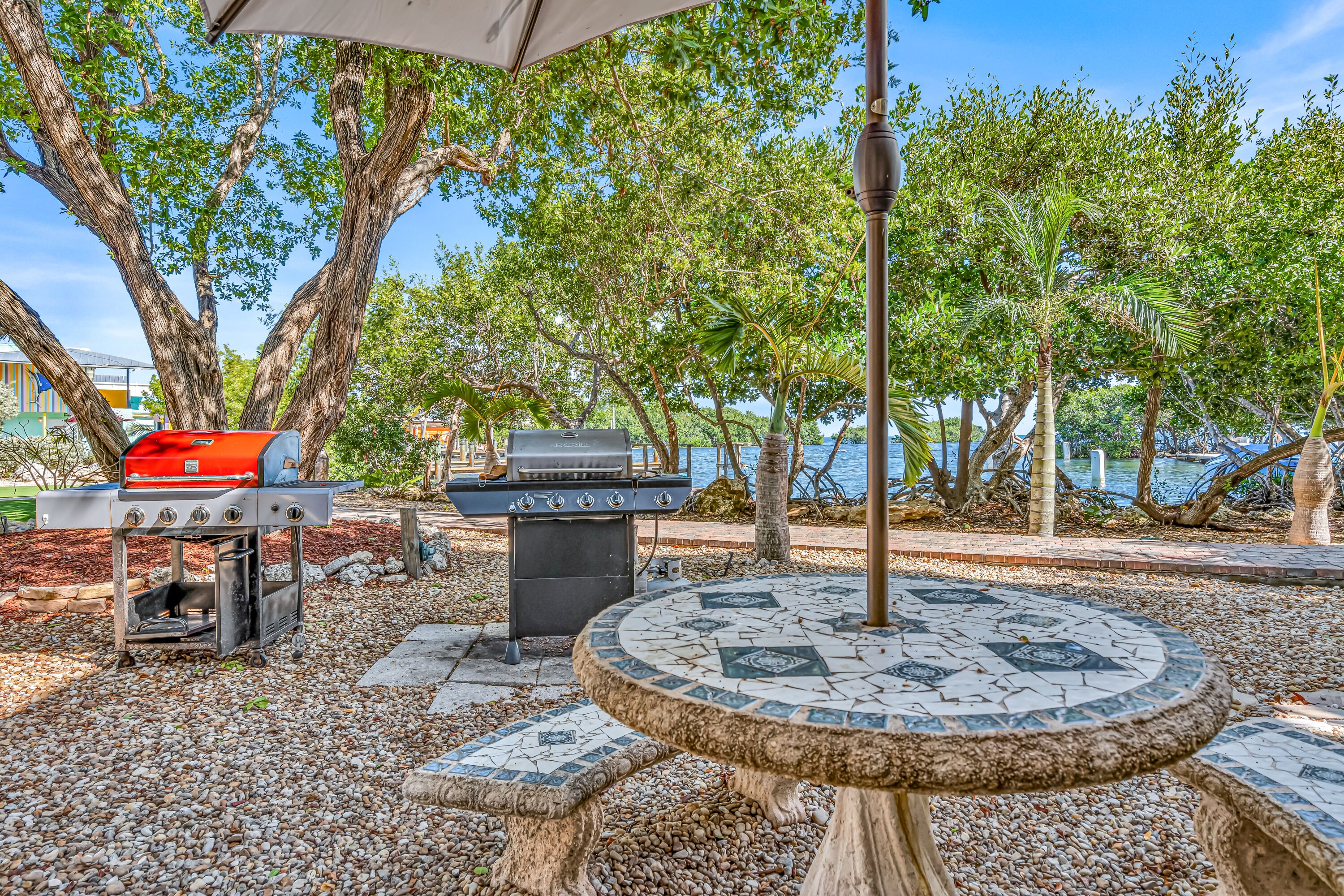 Een terras buiten met een barbecue, een betegelde tafel en uitzicht op het water.