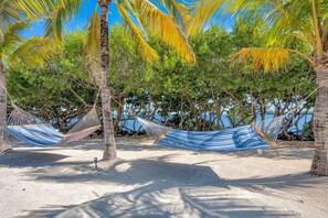 A beach with hammocks under palm trees, a sandy beach, and a clear blue sky. - Dove Creek Resort & Marina, Trademark Collection by Wyndham (Key Largo)