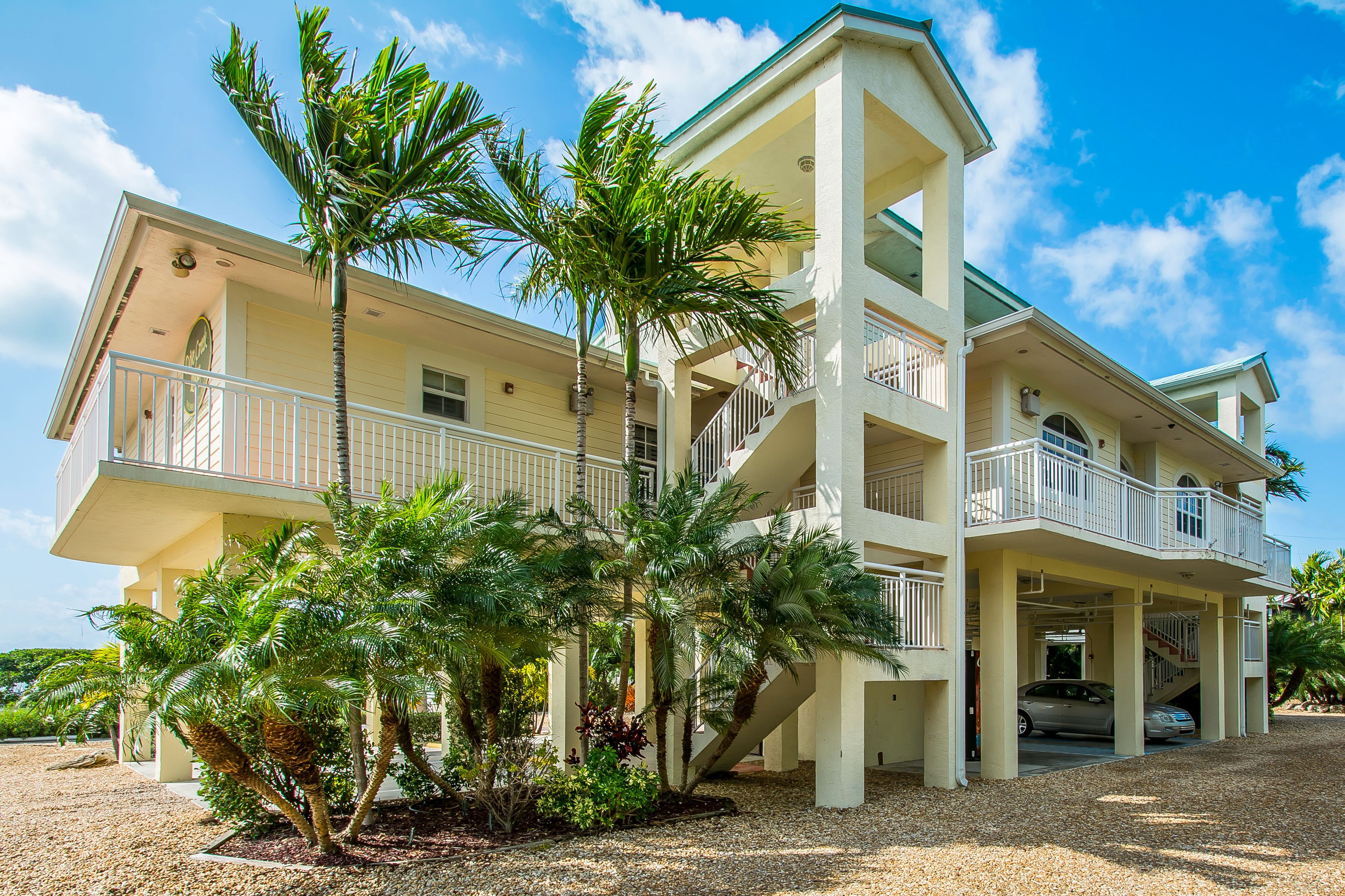 A multi-story building with balconies, a covered parking area, and palm trees.