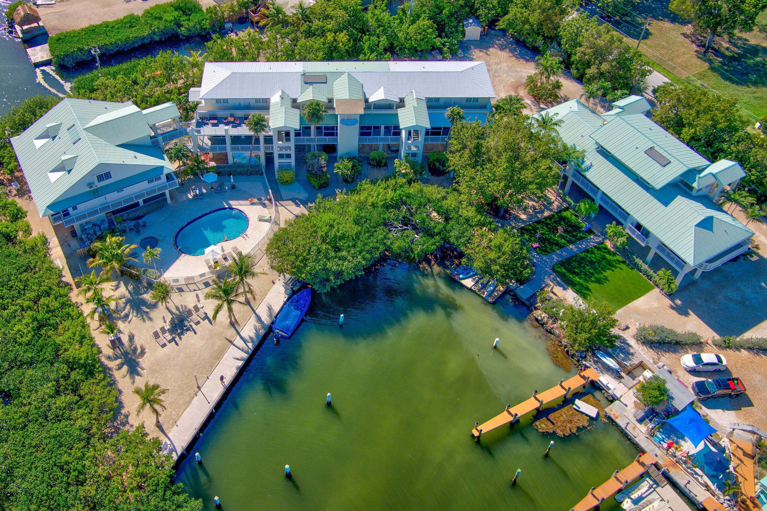 An aerial view of a resort with a swimming pool, multiple buildings, and a dock.