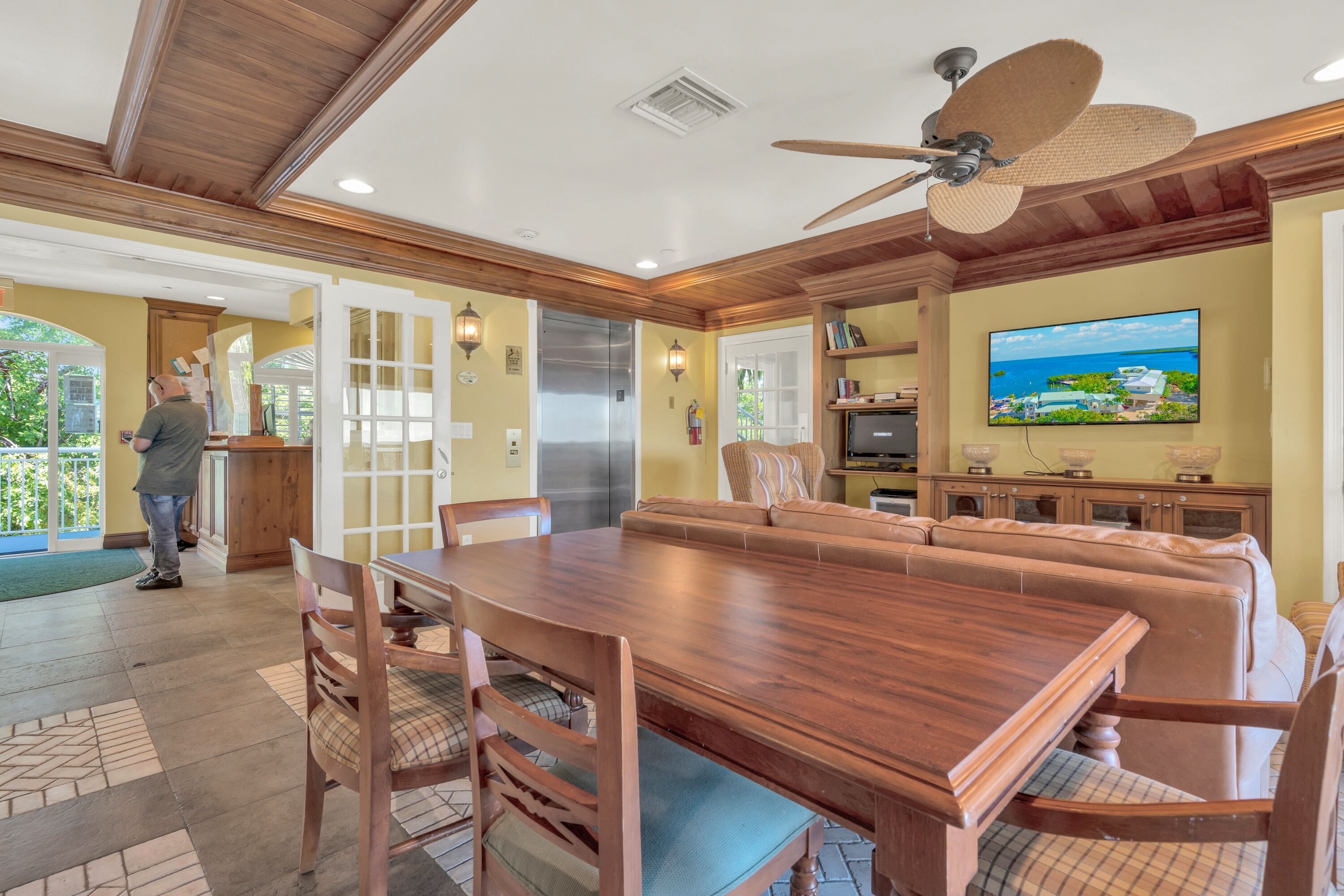 Tilava ruokailutila, jossa on puinen pöytä ja tuolit, kattotuuletin ja seinälle asennettu televisio.