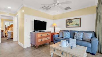 A living room with a television, a sofa, a coffee table, and a ceiling fan.