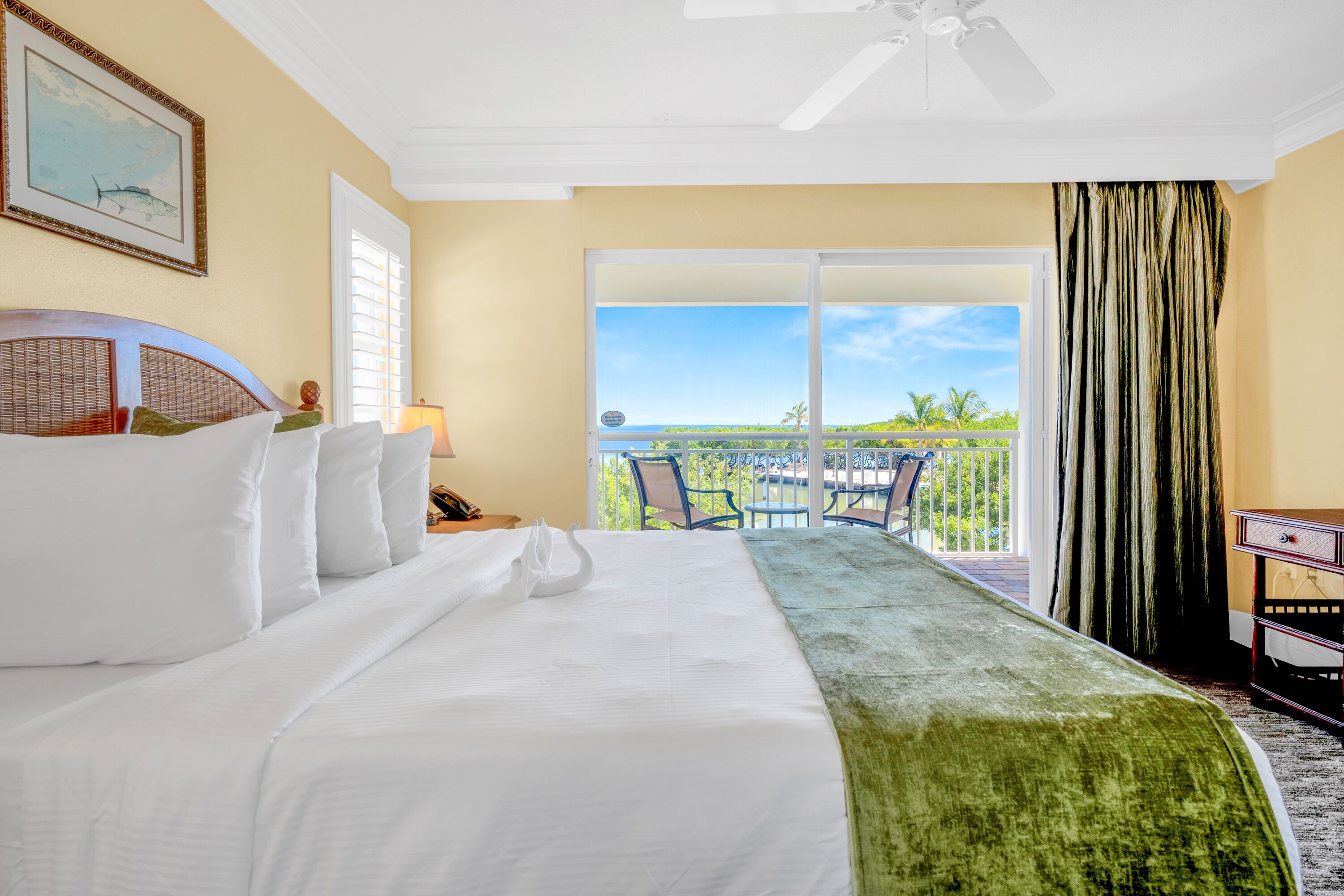 A hotel room with a large bed, a balcony with a view, and a ceiling fan.