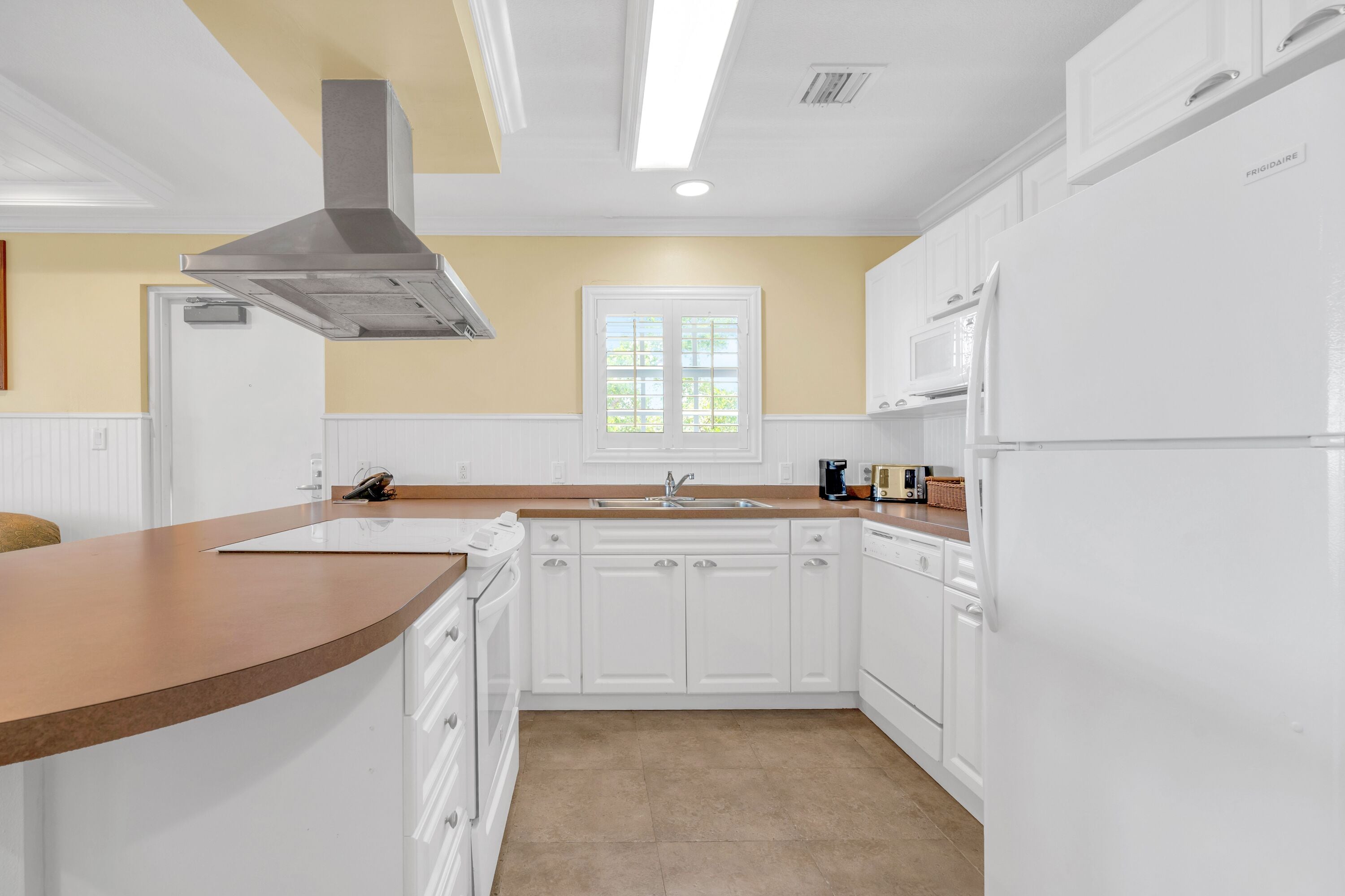 A modern kitchen with white cabinetry, a stainless steel range hood, a built-in oven, and a large refrigerator.