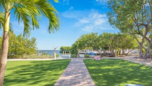 A paved pathway leading to a body of water, surrounded by lush greenery and palm trees. - Dove Creek Resort & Marina, Trademark Collection by Wyndham (Key Largo)
