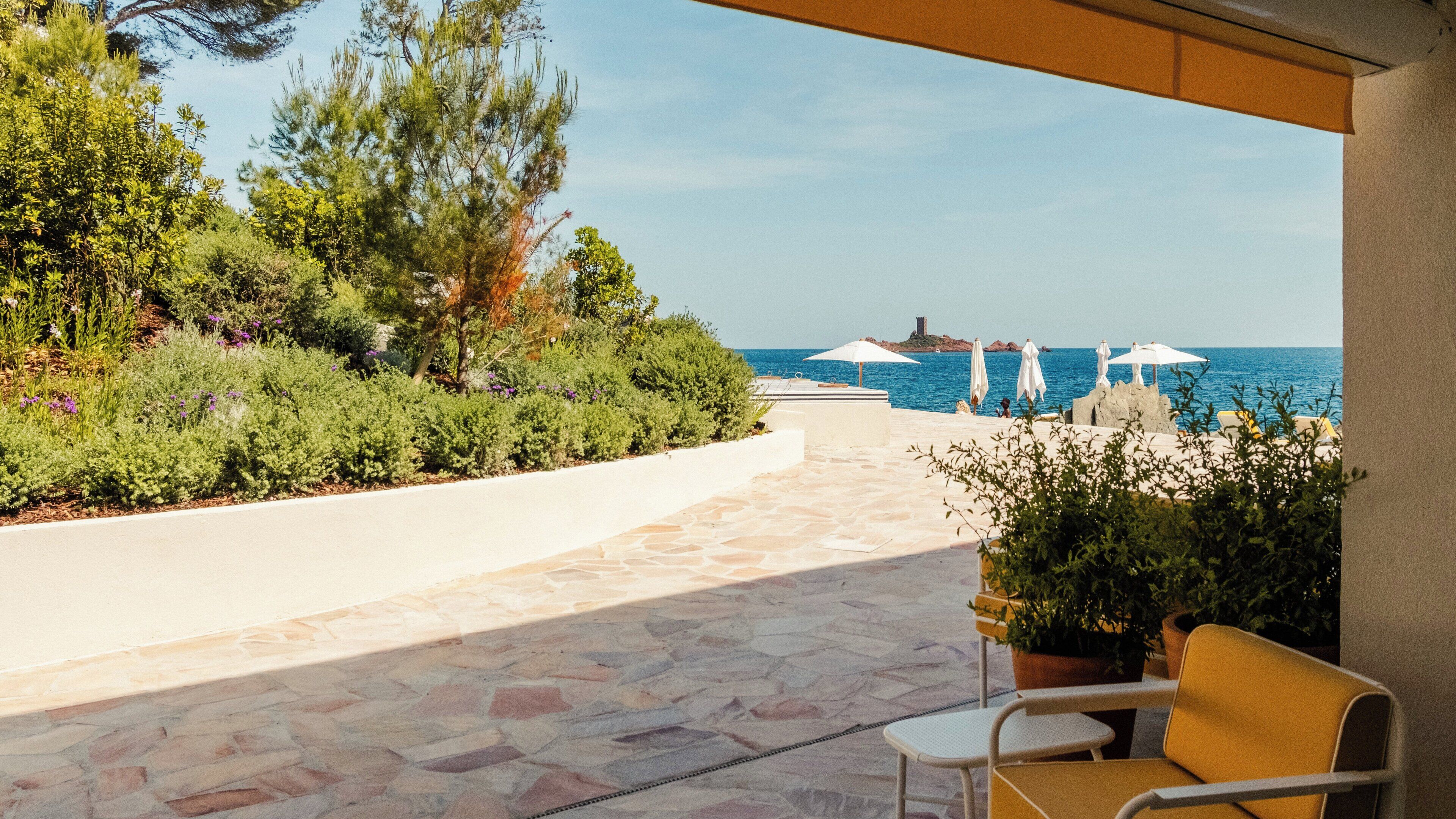 Une terrasse avec un sol en pierre, des sièges d’extérieur et des parasols, offrant une vue sur la mer.