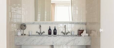 A bathroom with a marble sink, two faucets, a mirror, and two towel racks.