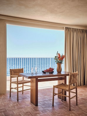 A balcony with a wooden table, two wicker chairs, a vase with flowers, and a view of the sea.