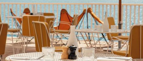 En restaurant ved havet med udendørs siddepladser, borde og stole med udsigt over havet.