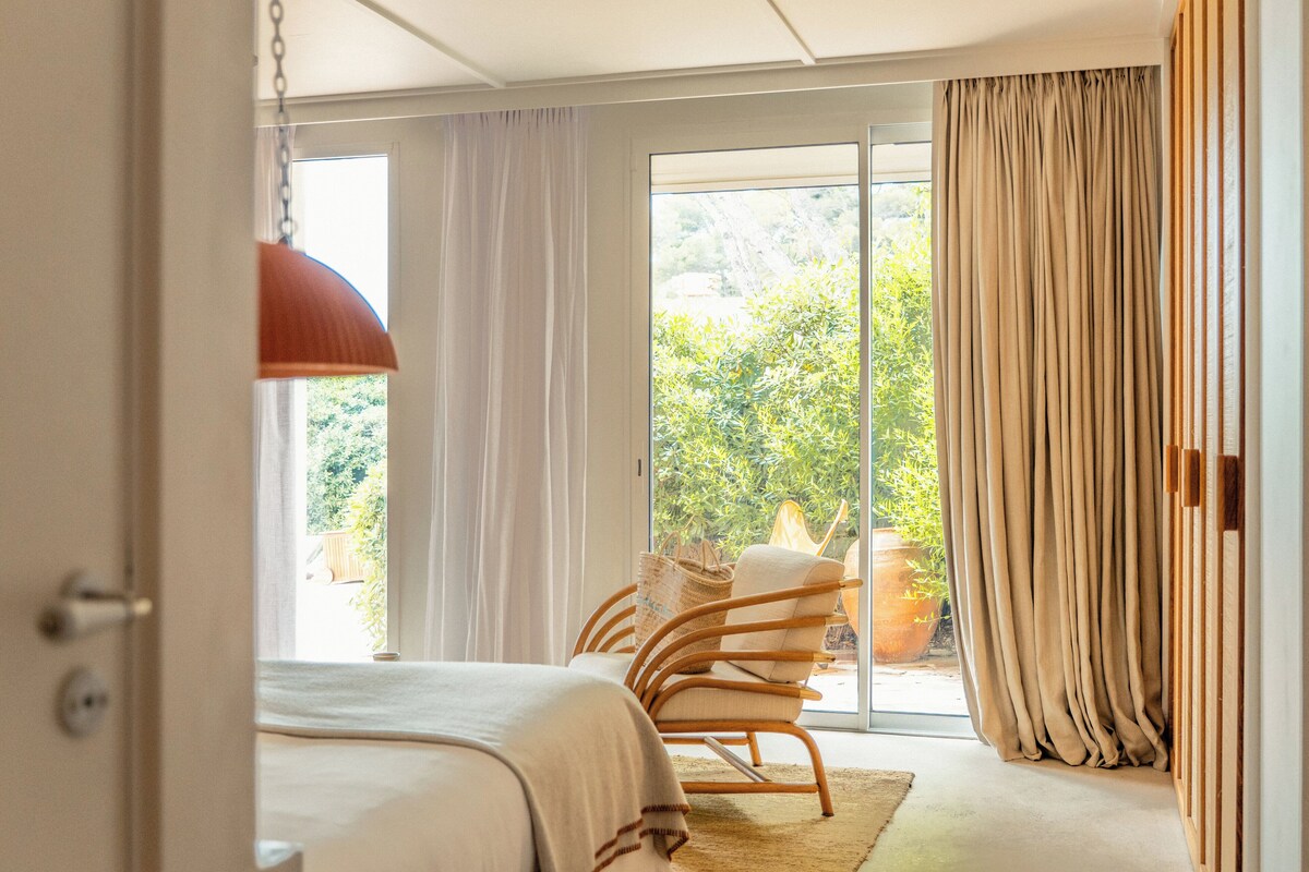 A bedroom with a bed, a chair, a large window, and curtains.