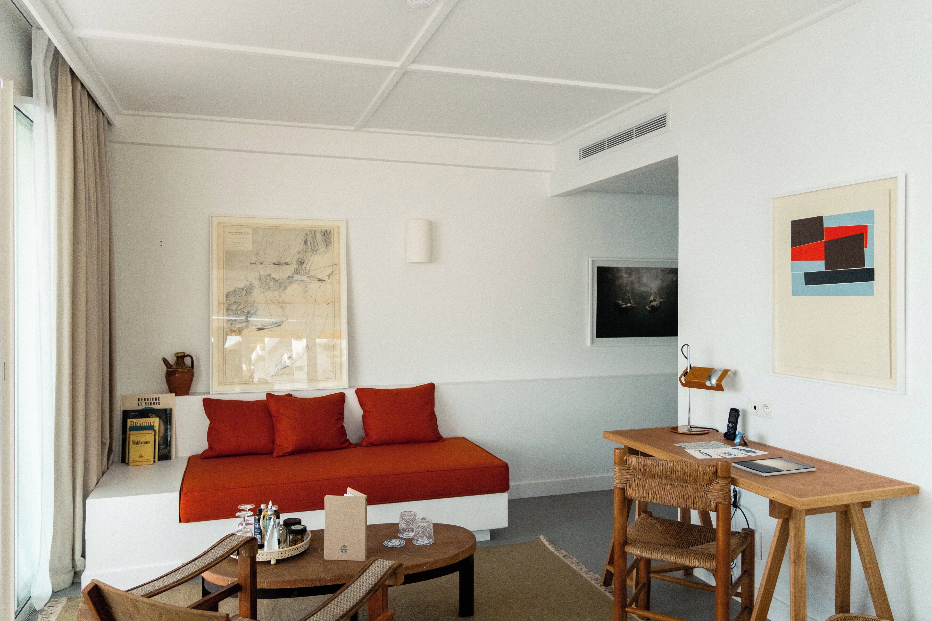 A modern hotel room with a white sofa, a wooden desk, and a large abstract painting.