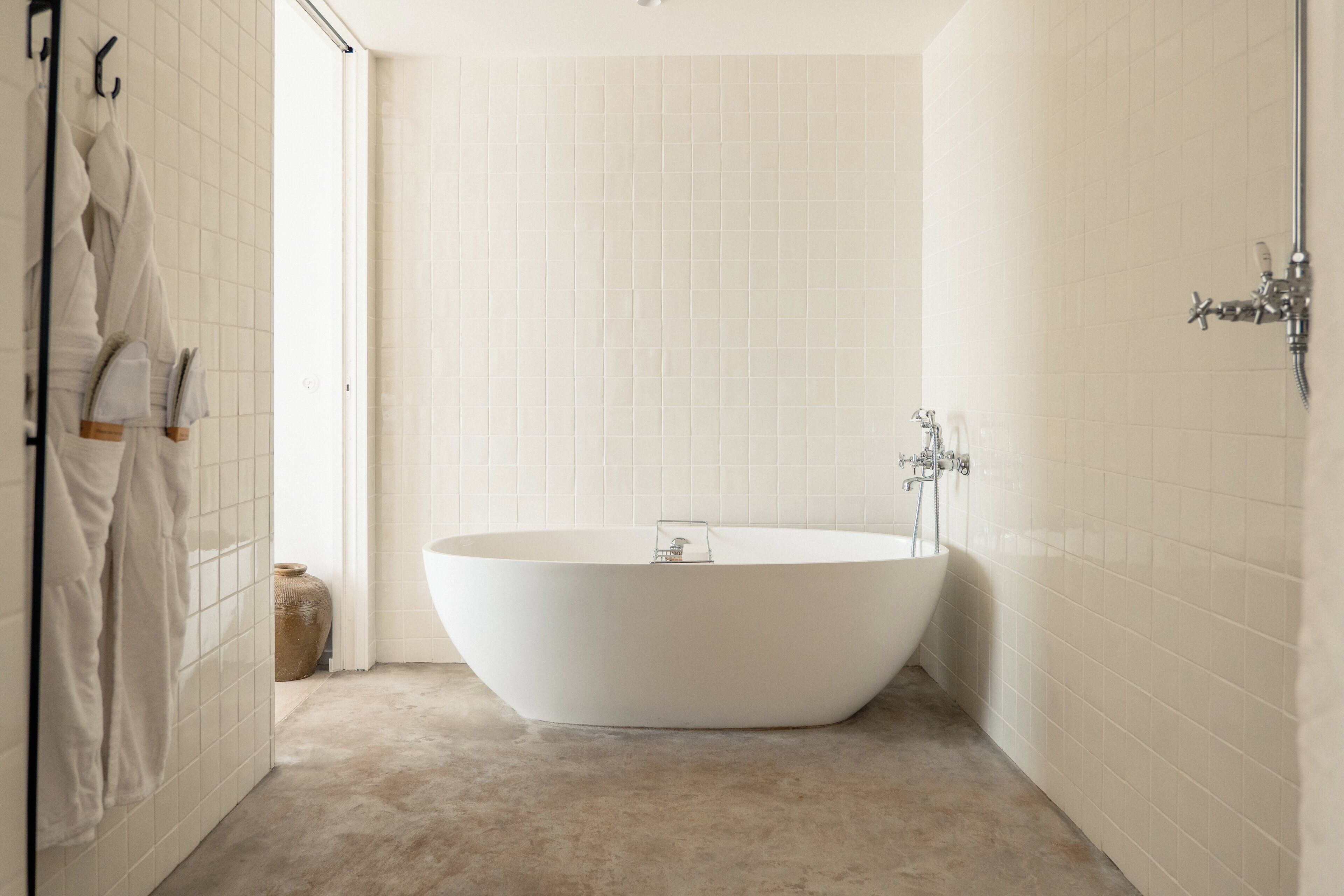 Une salle de bain moderne avec une baignoire sur pieds, des murs recouverts de carreaux blancs et un sol aux tons neutres.