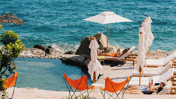 A beachside pool area with lounge chairs and umbrellas, surrounded by rocks and greenery. - Les Roches Rouges, a Beaumier hotel (Saint-Raphael)