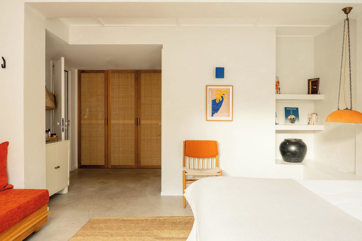 Quarto com cama, poltrona, guarda-roupa e prateleira com objetos decorativos.