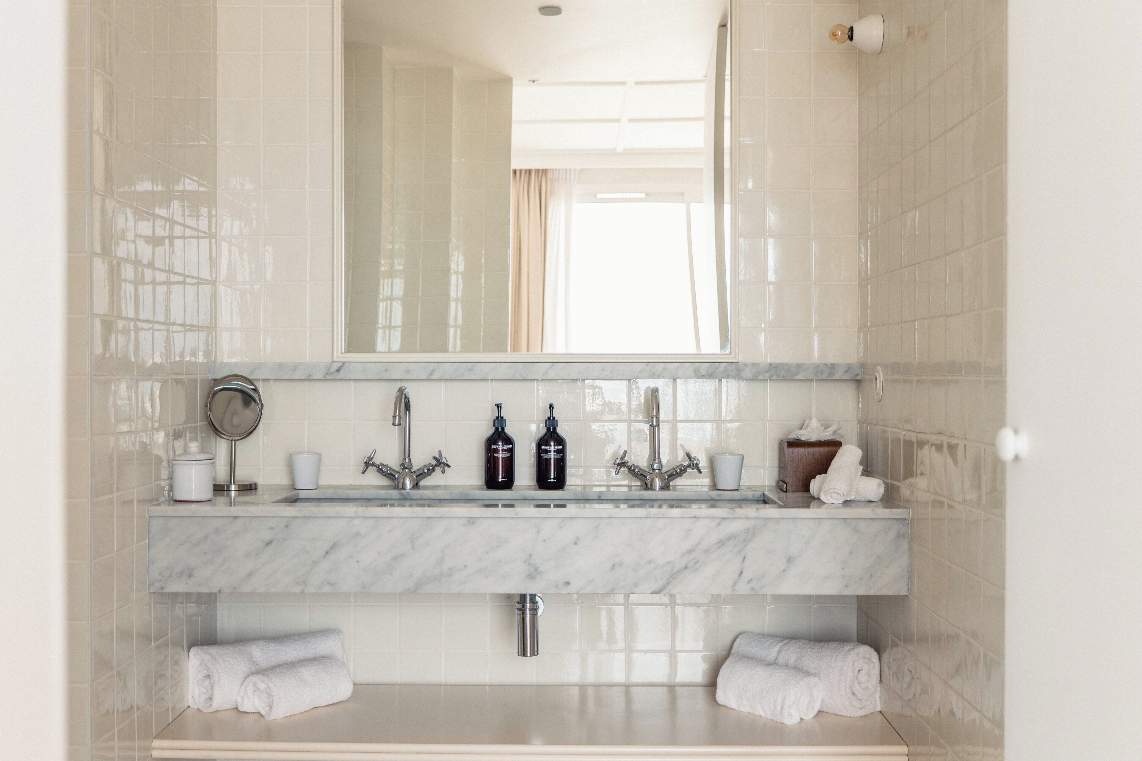 Une salle de bain avec un lavabo en marbre, deux robinets, un miroir et deux porte-serviettes.
