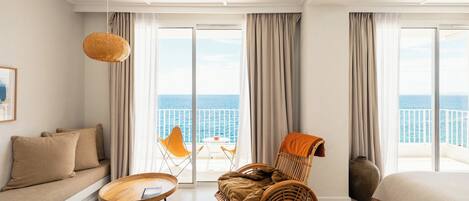 A hotel room with a balcony, a wicker chair, a sofa, and a bed.