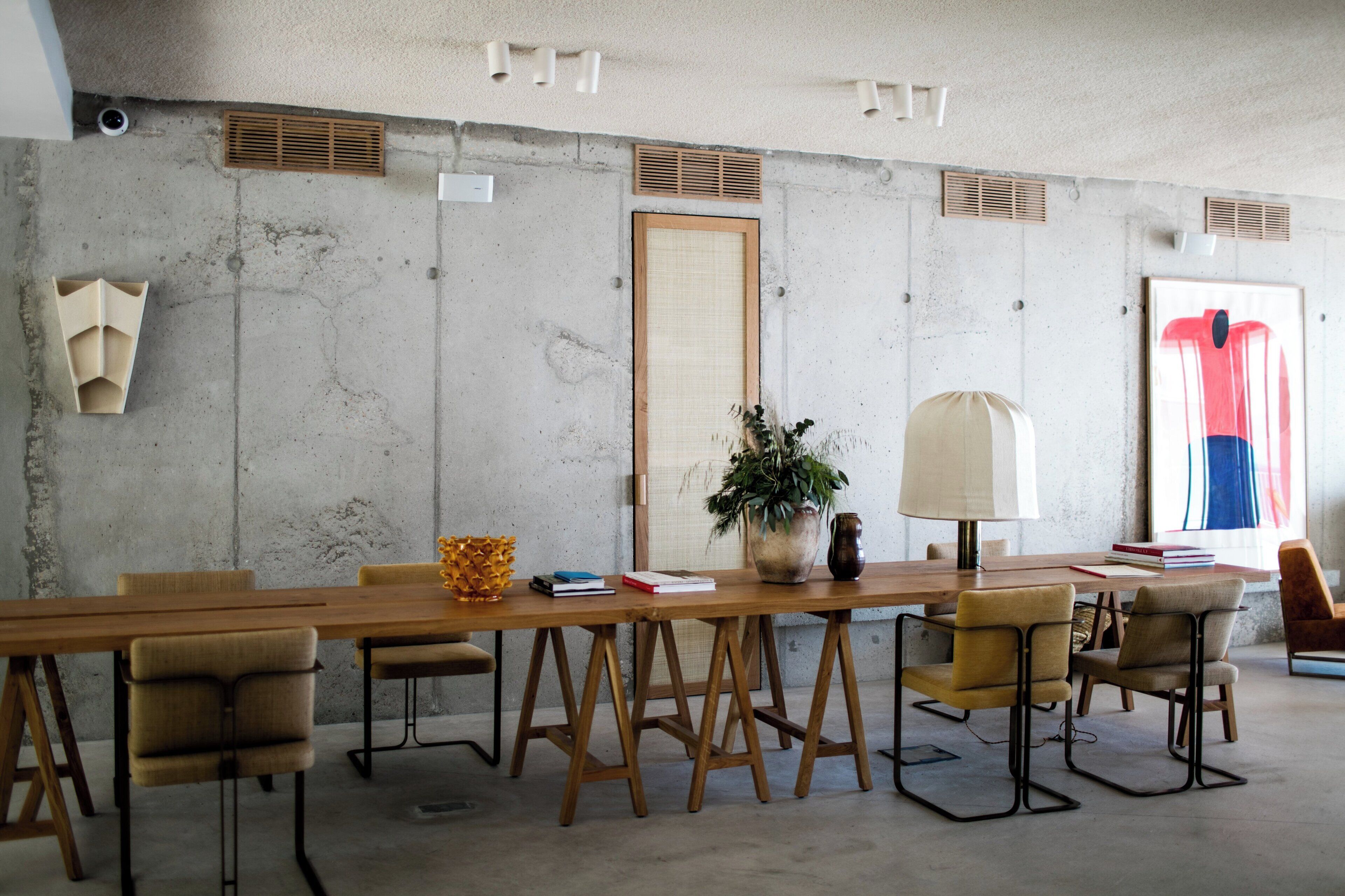A modern conference room with a long wooden table, several chairs, a potted plant, and a lamp.