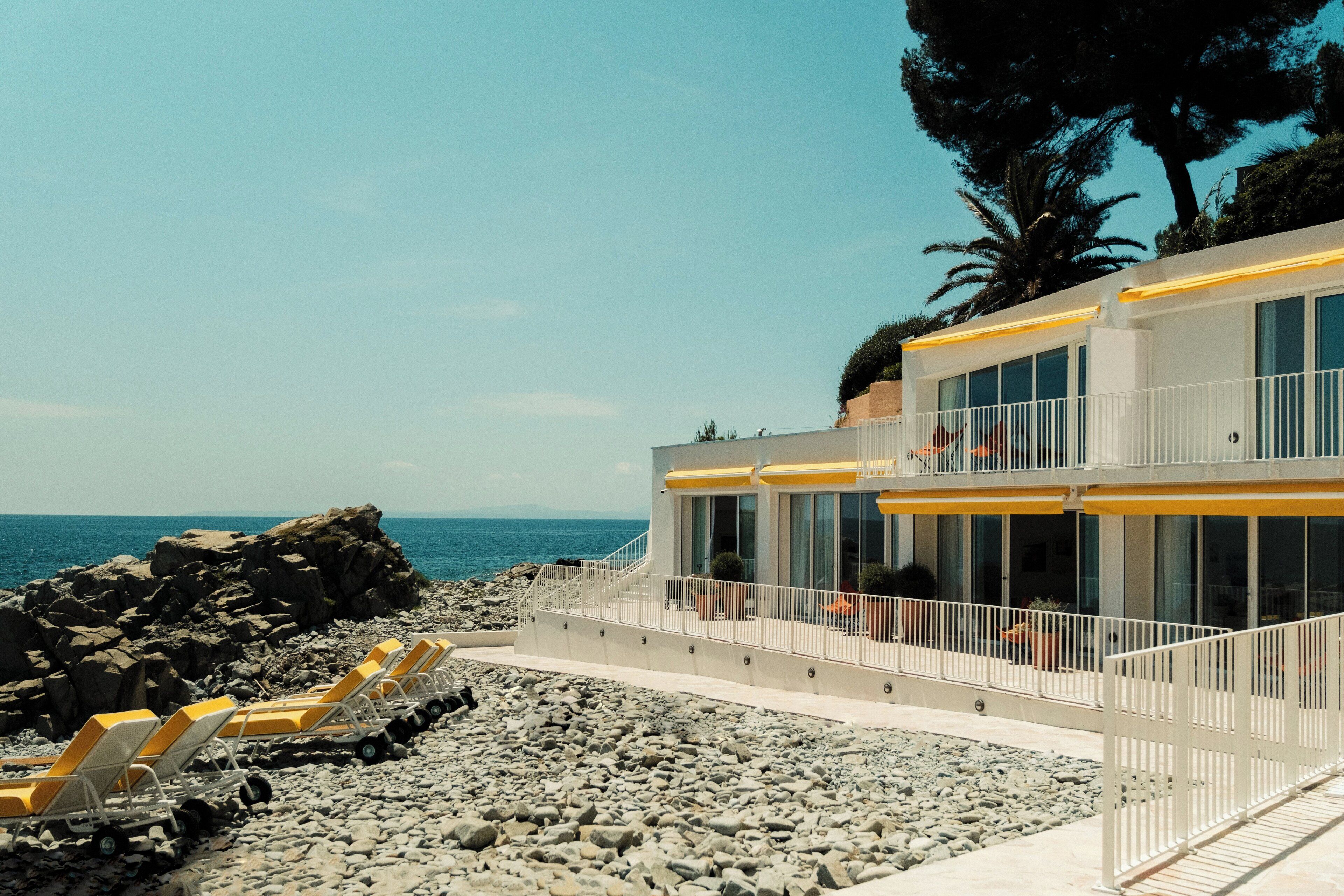A modern building with a balcony, a rocky beach, and a clear sky.