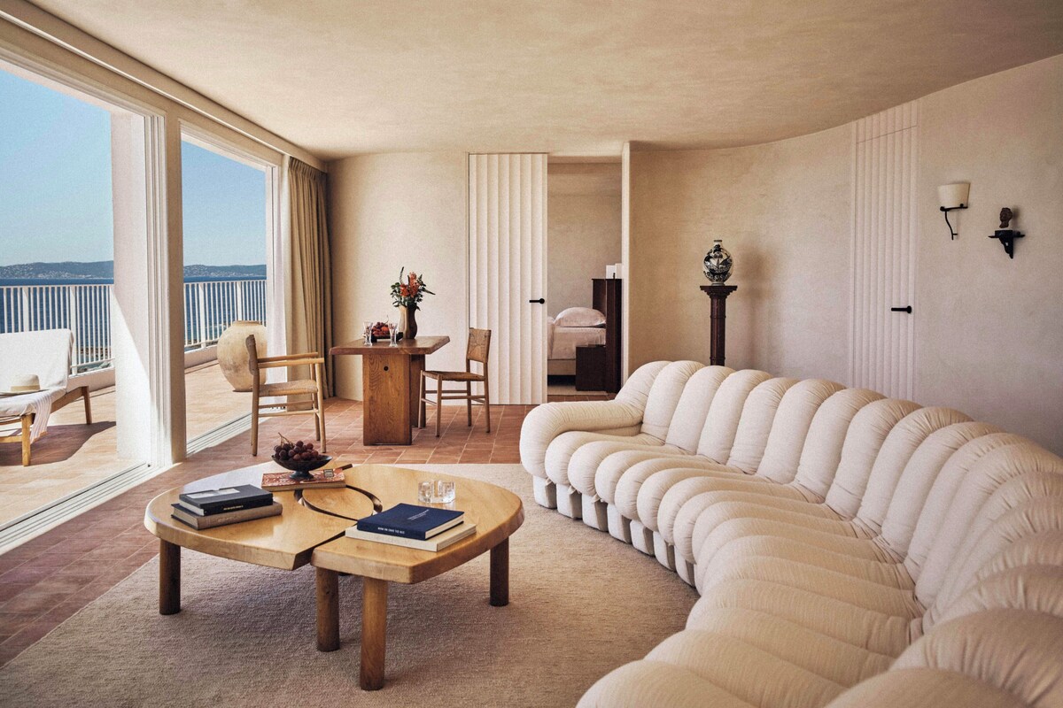 A spacious living area with a large window, a sofa, a coffee table, and a dining area.