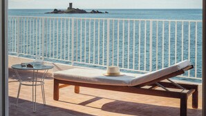 A balcony with a view of the sea, a lounge chair, a table, and a chair. - Les Roches Rouges, a Beaumier hotel (Saint-Raphael)