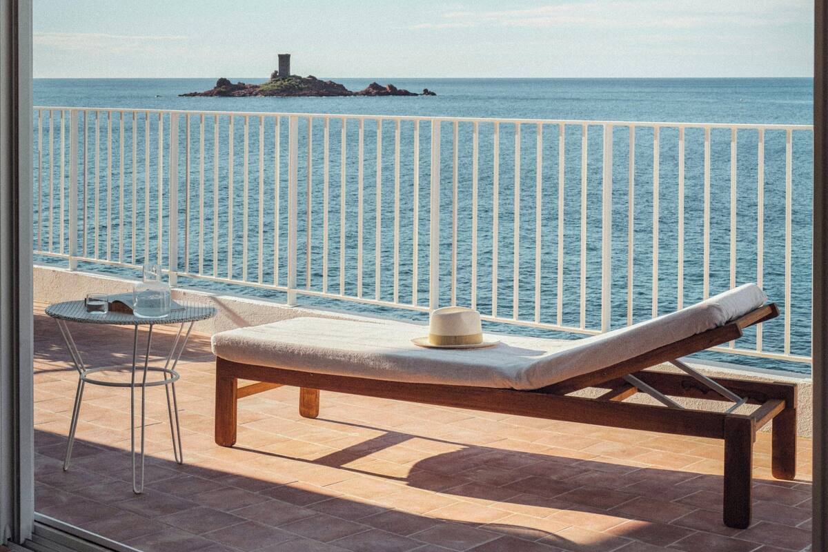 Varanda com vista para o mar, uma espreguiçadeira, uma mesa e uma cadeira.