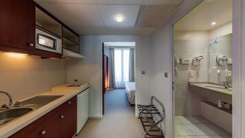 Une chambre d’hôtel compacte, dotée d’une kitchenette, d’une salle de bain avec douche et d’un lit en arrière-plan.