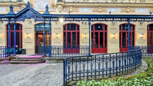 Un edificio histórico con ornamentales barandillas de hierro, una entrada adoquinada y un jardín de flores.