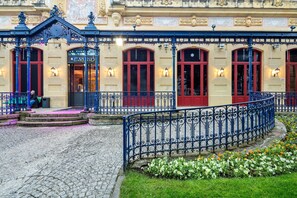 Un edificio histórico con ornamentales barandillas de hierro, una entrada adoquinada y un jardín de flores.