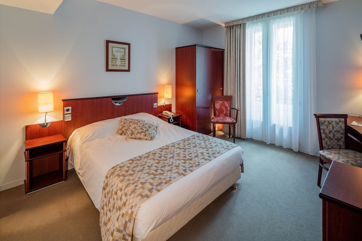 A hotel room with a bed, bedside lamps, a wardrobe, a chair, and a desk.