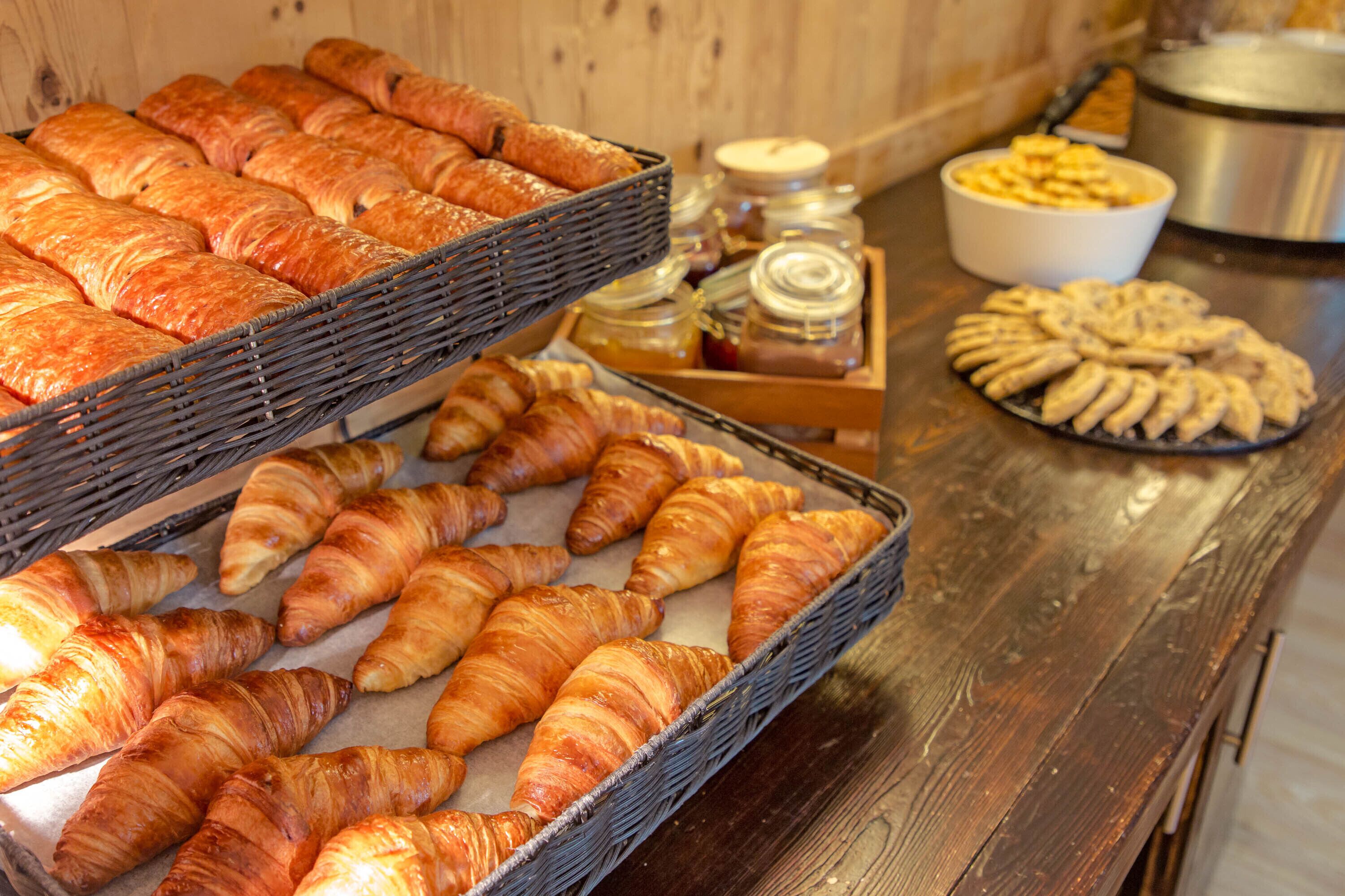 A variety of baked goods including croissants and pastries displayed in baskets and on trays.