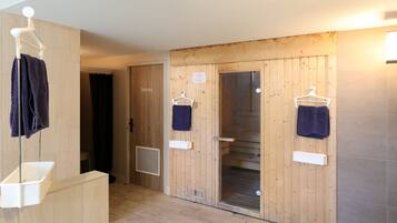 A sauna room with wooden walls, two towel hooks, and a white sink.