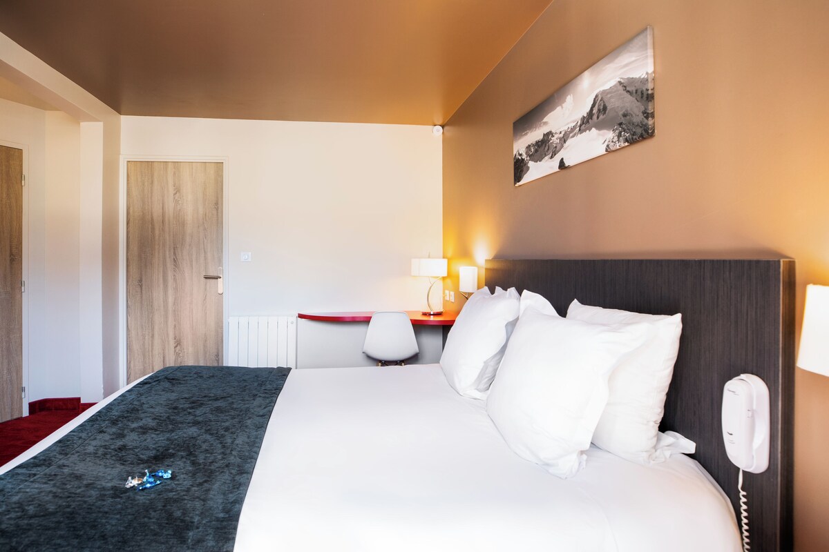 Habitación de hotel con cama, escritorio, silla, teléfono y un cuadro en la pared.