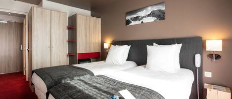 A hotel room with two beds, a wardrobe, a bedside table with a lamp, a phone, and a picture on the wall.