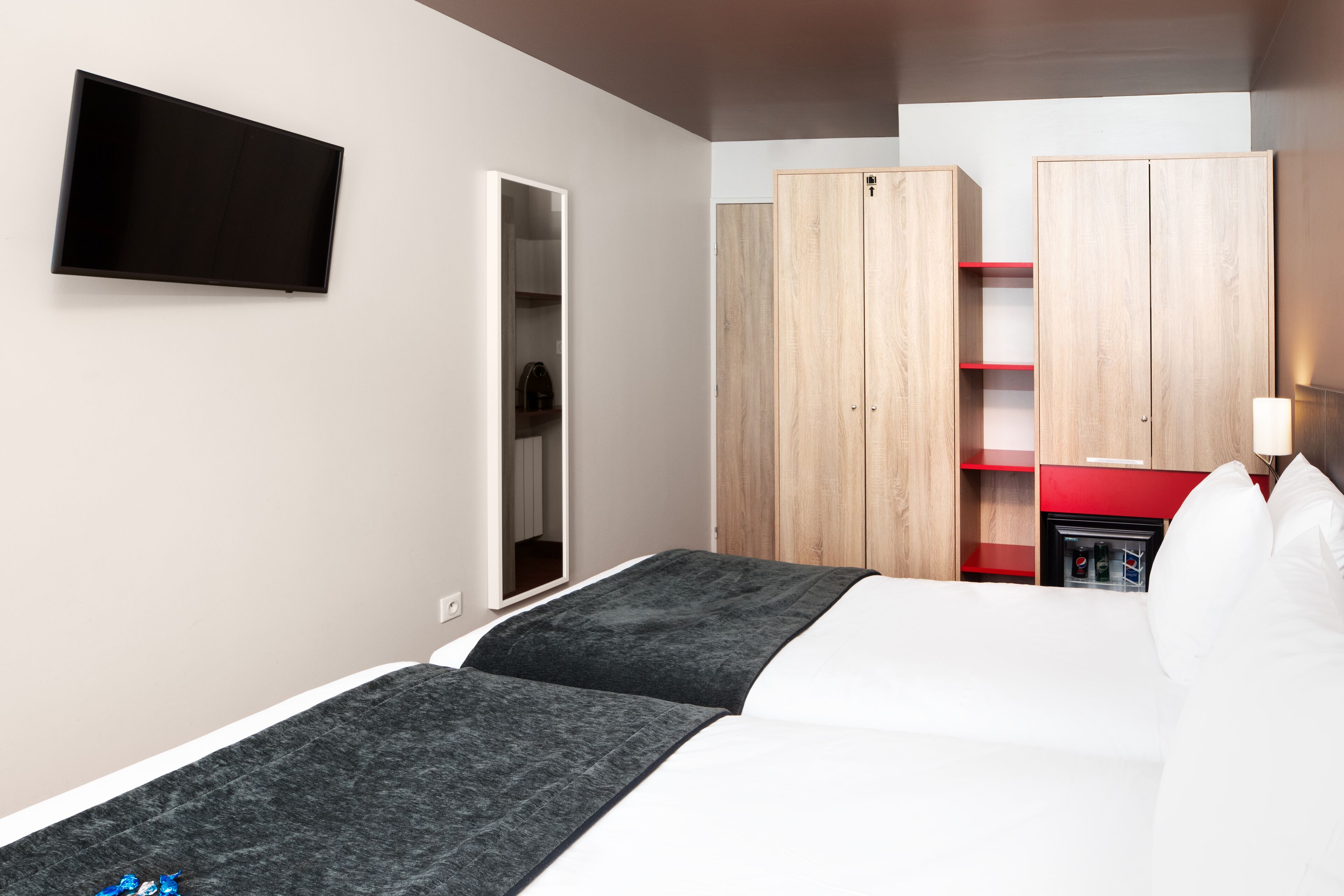 A hotel room with two beds, a TV, wooden wardrobes, and a red minibar.
