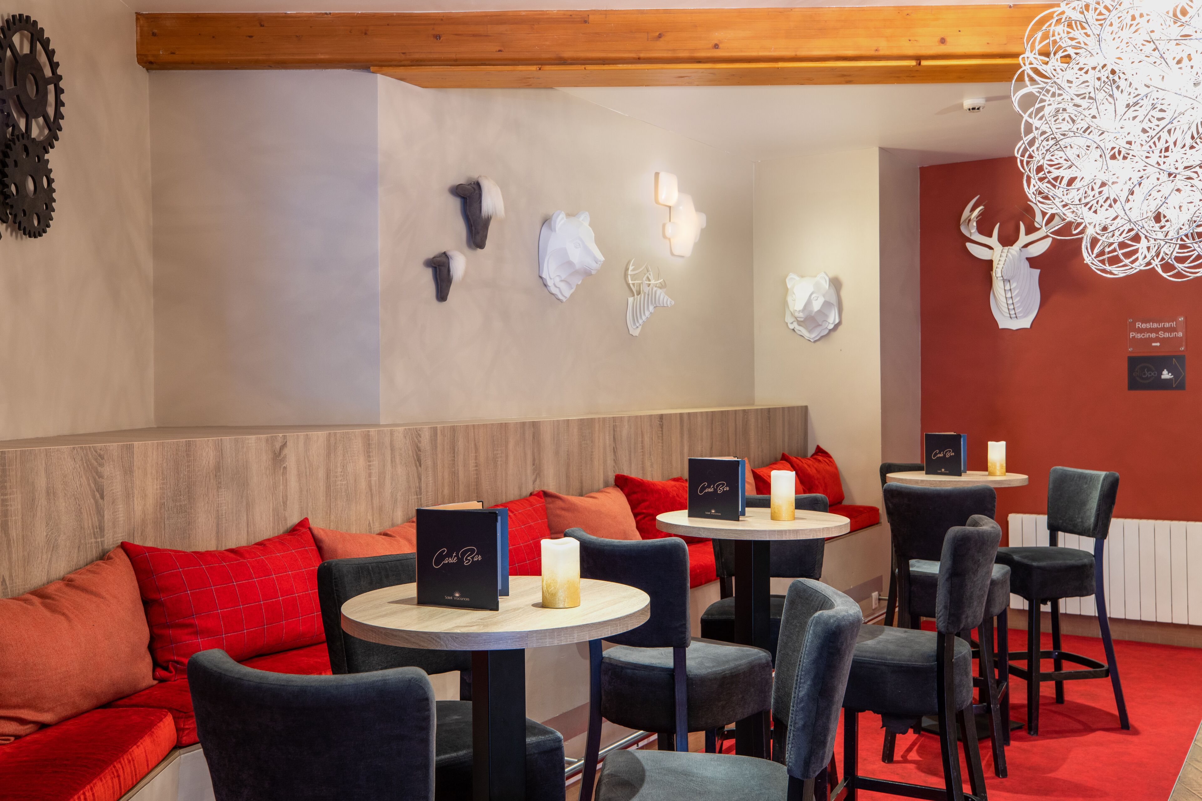A restaurant interior with round tables, red and black upholstered seating, and decorative wall art including animal skulls and a chandelier.