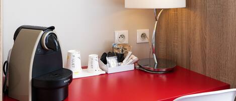 A red desk with a coffee maker, a lamp, and a cup holder with coffee cups and a bag of coffee.