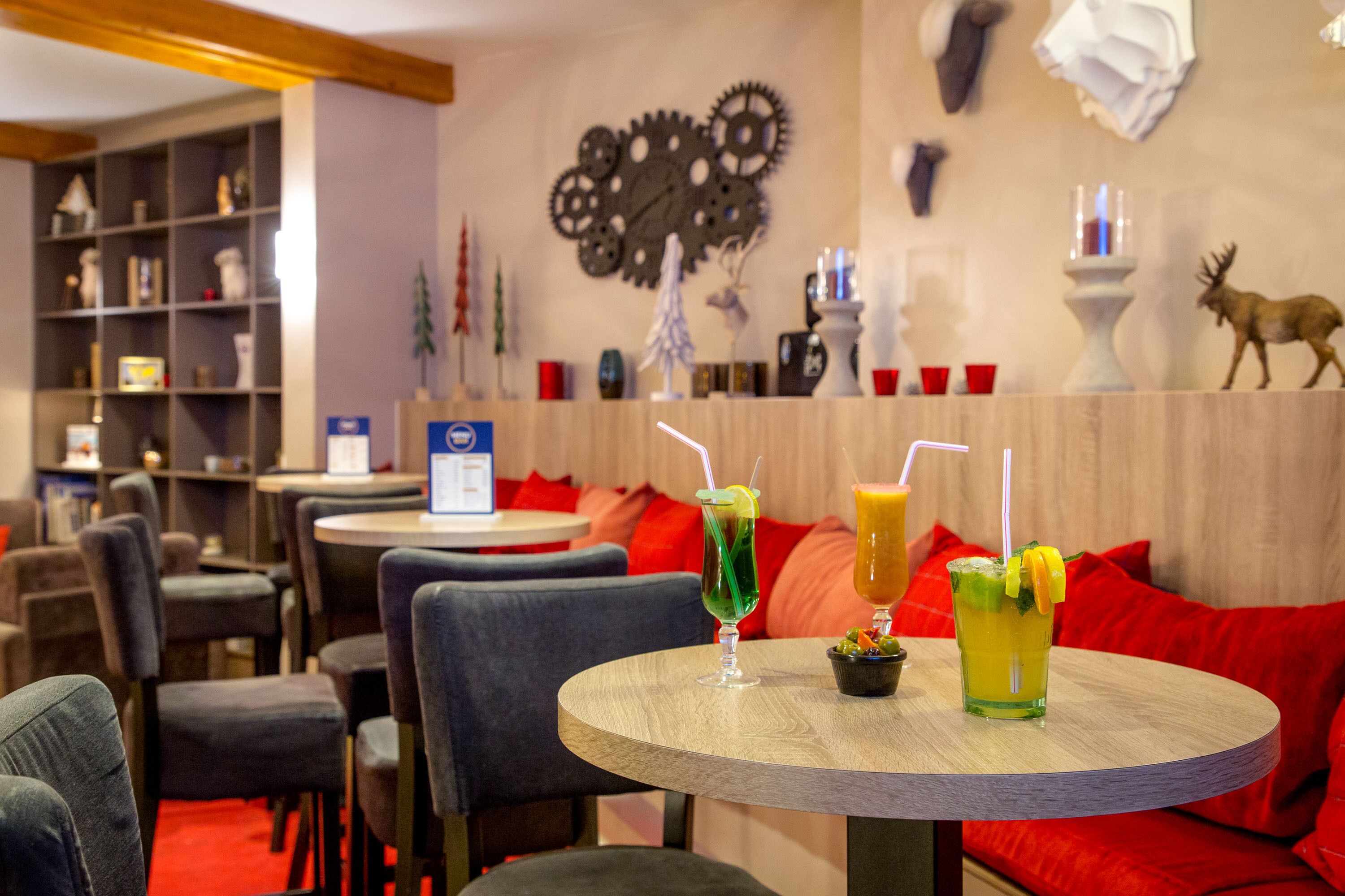 Un restaurant avec des tables rondes, des chaises à revêtement rouge et un mur décoré d’engrenages et de têtes d’animaux.